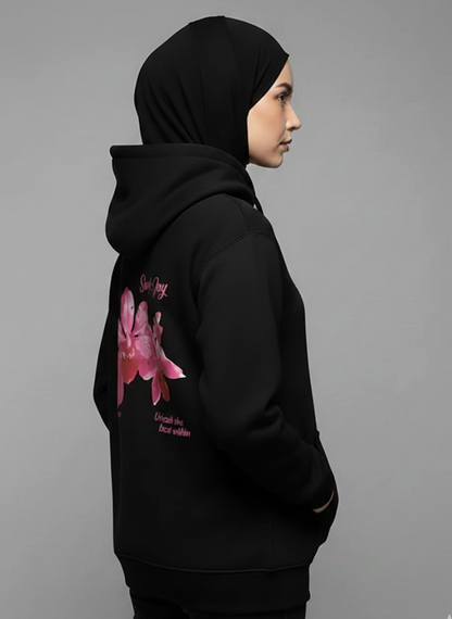 Person wearing a black hoodie with a pink graphic on the back against a gray background